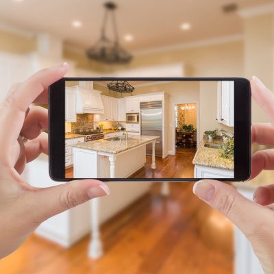 Female Hands Holding Smart Phone Displaying Photo of Kitchen Behind.